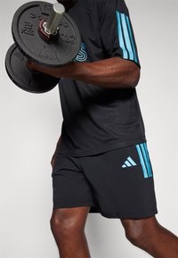Black mesh athletic shirt with blue stripes, paired with black shorts. Holding a weighted dumbbell, showing muscular arm detail.