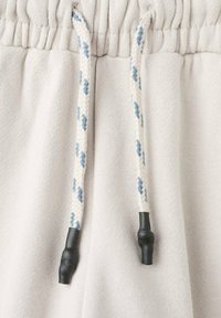 Tissu gris clair avec une taille élastique ; présente des cordons tressés avec des éclats bleus et des embouts en plastique noir pour un ajustement.