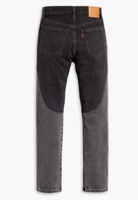 Jean en denim bicolore noir et gris vu de dos avec un design patchwork, deux poches arrière, passants de ceinture et une étiquette de marque en cuir beige.