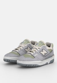 Les baskets New Balance 550 grises et vertes présentent une tige en suède et en mesh, une semelle en caoutchouc légère, ainsi qu'un logo sur le côté et la languette.
