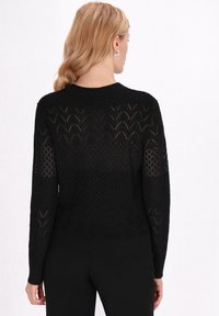 Pulover negru tricotat cu un model texturat care evidențiază diamante și chevrone, având mâneci lungi și guler rotund.