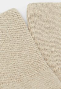 Beige ribstrikkede sokker med blød tekstur, der har en foldet manchet og en sømløs topkant for komfort. Detaljeret syning synlig overalt.