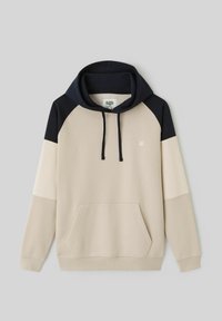 Sweat-shirt à capuche présentant un corps crème avec des accents bleu marine et beige clair, une poche avant et des cordons de serrage noirs. Texture douce, coupe décontractée.