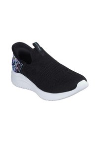 Zapatilla negra tipo slip-on con parte superior de punto transpirable, suela de goma blanca y un acento floral colorido en el talón.