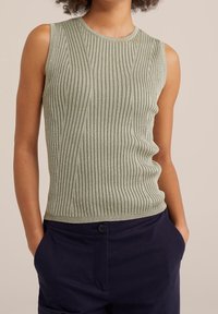 Ljusgrön ärmlös ribbad stickad topp med rund halsringning, försedd med ett strukturerat mönster och en smal passform, kombinerad med mörka byxor.