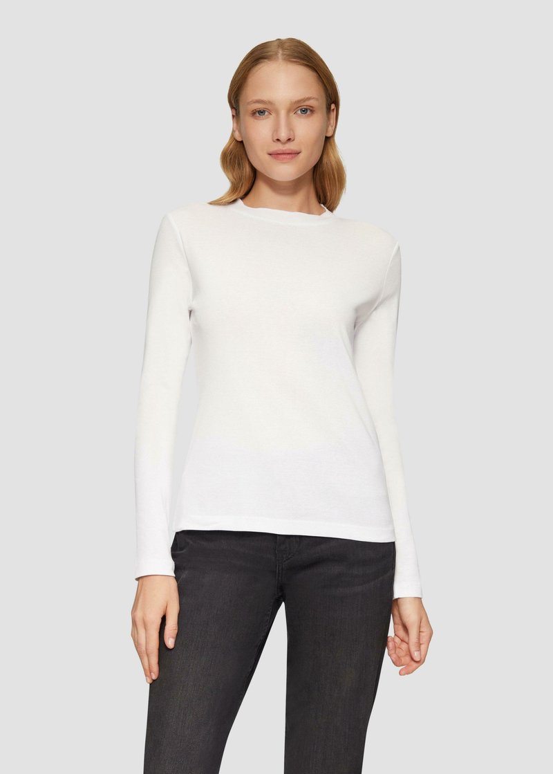 Witte lange mouw shirt met een ronde hals, gemaakt van een gladde, lichte stof. Gecombineerd met donkere zwarte jeans. Eenvoudig en aangesloten ontwerp.