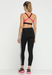 Czarne legginsy z białymi bocznymi paskami w połączeniu z różowym sportowym biustonoszem z krzyżującym się tyłem. Teksturowany materiał o kontrastujących kolorach.