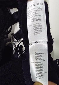 Étiquette de vêtement indiquant les instructions de lavage et la composition du tissu : 60 % polyamide, 35 % polyester, en plusieurs langues, sur un vêtement en dentelle noire.