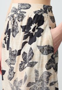 Bloemrijke rok met een beige basis en gedurfde zwarte bloemenpatronen. Heeft een soepele textuur en zijzakken voor extra functionaliteit.