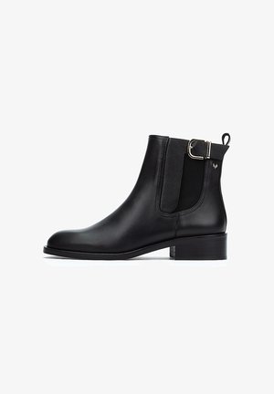 Botines de cuero negro con paneles elásticos laterales, un pequeño tacón cuadrado y una hebilla metálica decorativa en el costado. Textura suave, punta afilada.