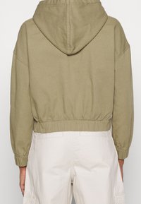 Olive green cropped hoodie with a drawstring hood, elastic waistband, and ribbed cuffs. Made from soft, textured fabric.