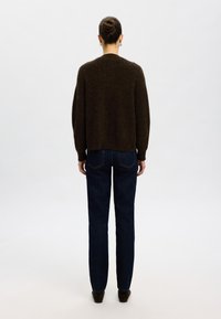 Temno rjava pletena majica z ohlapnim krojem, spušenimi rameni in skrajšanim robom, v kombinaciji s temno modrimi ravnimi hlačami.