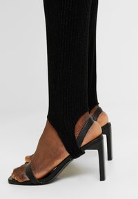 Svarta klacksandaler med öppen tå och ankelrem. Har en elegant design och slät yta, kombinerat med ruggad svart textil.