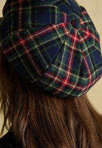Wełniany beret w kratę w odcieniach granatu, zieleni, czerwieni i żółci, z guzikową ozdobą na górze i wyraźnie zarysowanym kształtem.