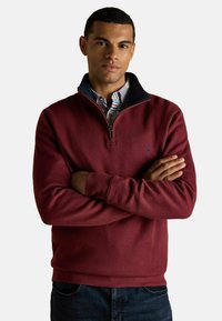 Bordeaux fleece half-zip sweater met een marineblauwe kraag, met een subtiel logo op de borst en een relaxed fit. Draagt over een geruit shirt.