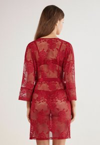 Czerwona koronkowa szlafrok z kwiatowymi wzorami, rękawami o długości do połowy przedramienia i paskiem w talii. Przezroczysty materiał z długością do połowy uda.
