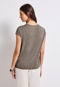 Šedé triko s krátkým rukávem, uvolněný střih, hladká textura a zakulacený spodní lem. Zadní pohled ukazuje jemný šev podél ramen.