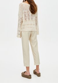 Pull tricoté couleur crème avec design ajouré, coupe ample, associé à un pantalon beige fuselé et des chaussures slip-on texturées avec un motif tissé.