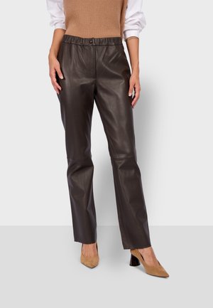 Pantalons en cuir marron à coupe ajustée, avec une fermeture à bouton à l'avant et une taille élastique. Assortis à des chaussures à talons beiges.