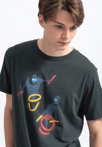 T-shirt nera in cotone con una grafica colorata di due figure con occhiali blu, circondate da anelli rossi e gialli. Maniche corte, girocollo.