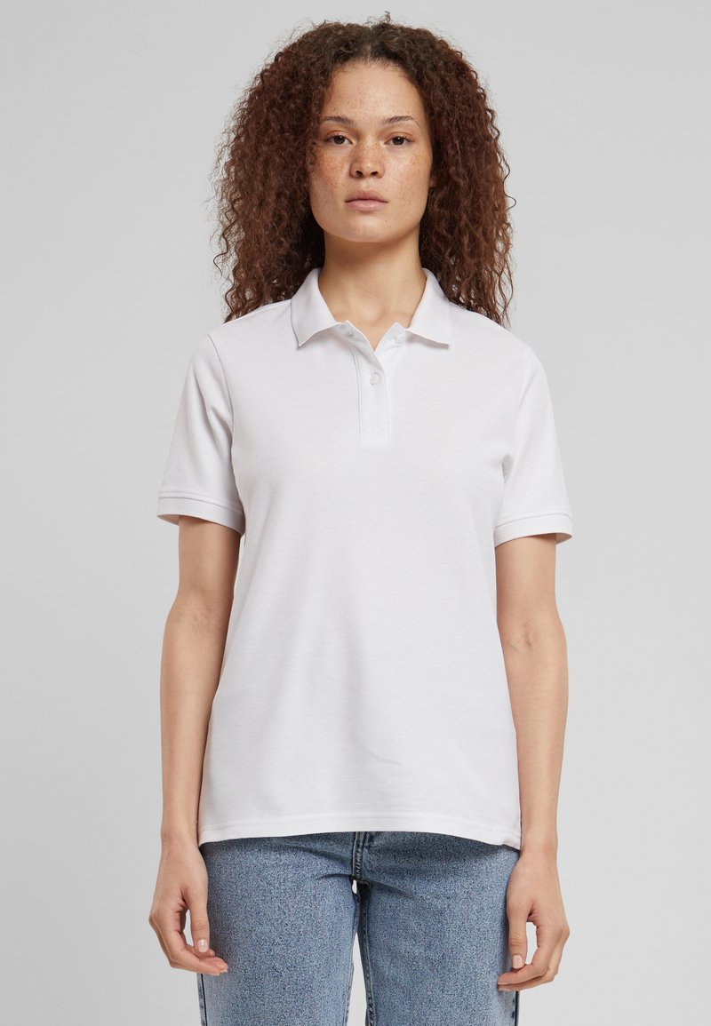 Hvid polo skjorte med krave og tre knapper, lavet af glat stof. Korte ærmer, afslappet pasform, parret med lys blå jeans.
