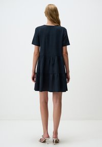 Ciemnoniebieska, krótko rękawowa sukienka o warstwowym designie i luźnym kroju, wykonana z miękkiego materiału. Długość do kolan z okrągłym dekoltem.