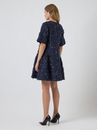 Tamsiai mėlynas tekstūruotas suknelė su trumpomis rankovėmis, išryškinančiomis suplėšytus akcentus ir platėjančiu siluetu. Dėvima su juodais stiletto kulnais.