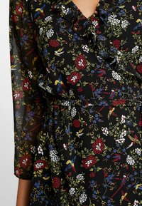 Vestido negro con estampado floral que presenta un escote con volantes, con patrones de rosas rojas, flores azules y pájaros amarillos sobre una tela transparente.