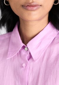 Light pink collared shirt with buttons, featuring a smooth texture and subtle sheen. Close-up view focuses on collar and neckline details.