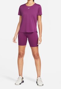 Lila sporttopp med korta ärmar och rund halsringning, kombinerad med lila åtsittande shorts. Nike-logotypen syns på toppen.