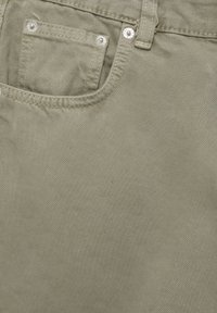 Gros plan sur un tissu en denim vert olive clair montrant les détails de la poche avant, des rivets, des coutures et des passants de ceinture.