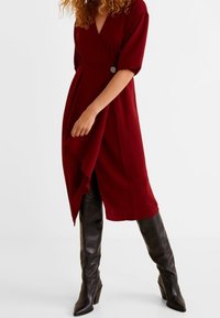 Burgundy merenneule, jossa on V-pääntie, puolihihat, sivunappidetalji ja epäsymmetrinen helma; hieno rakenne ja monikäyttöinen pituus.