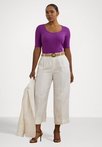 Top viola a costine con scollatura a barca, pantaloni beige a gamba larga e una cintura intrecciata. Sono inclusi anche sandali marroni con cinturini e un blazer chiaro.