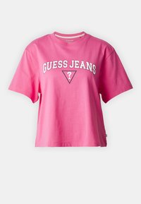 Růžové bavlněné tričko s krátkými rukávy, s bílým logem "GUESS JEANS" v stylizovaném písmu a trojúhelníkovou grafikou pod ním.