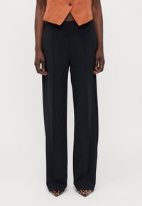Zwarte, wijde broek met een hoge taille, met een gladde textuur en strakke lijnen. Gepaard met puntige, leoprint hakken.