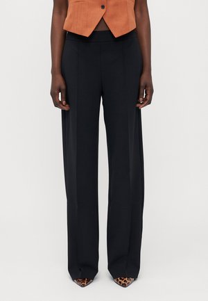 Black, wide-leg trousers with a high waistband, featuring a smooth texture and clean lines. Paired with pointed, leopard-print heels.