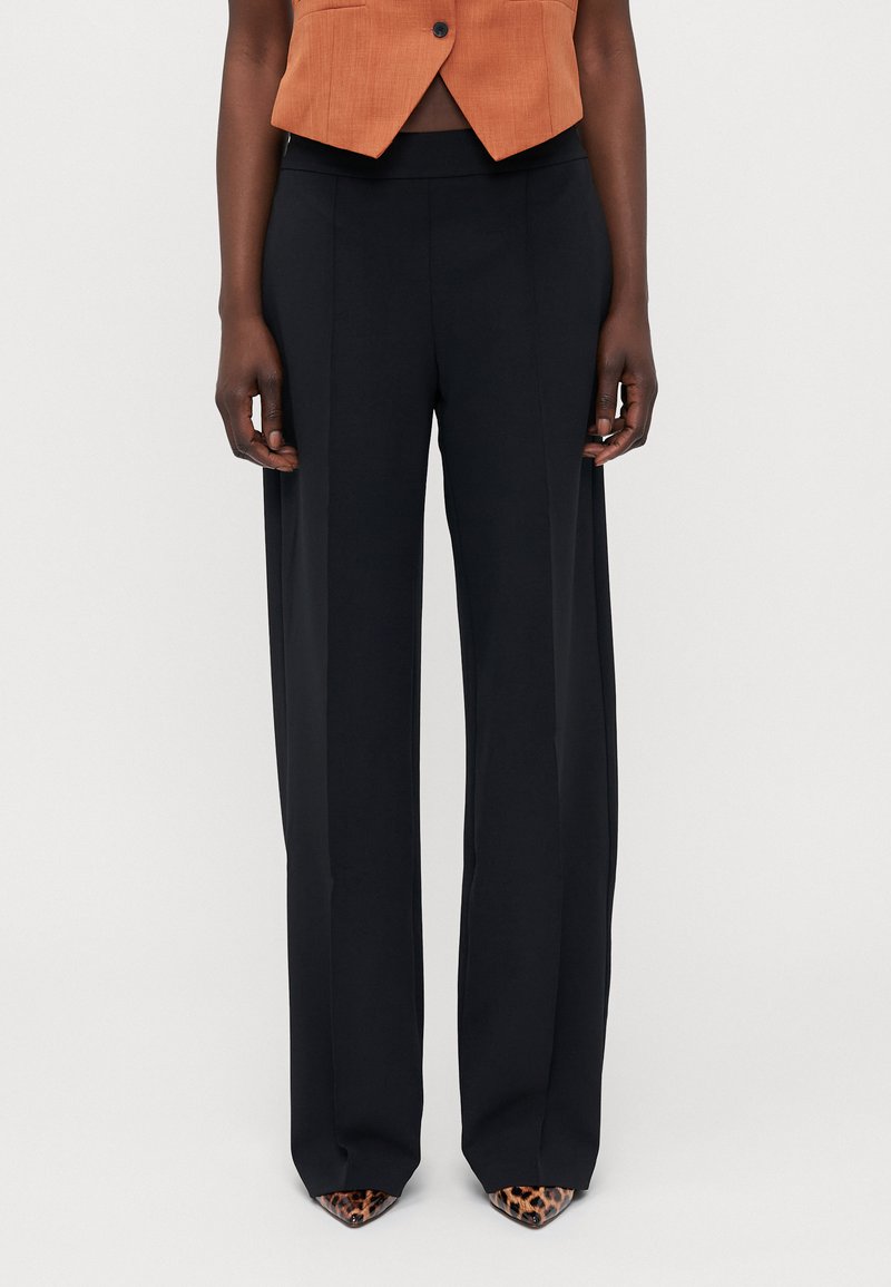 Zwarte, wijde broek met een hoge taille, met een gladde textuur en strakke lijnen. Gepaard met puntige, leoprint hakken.
