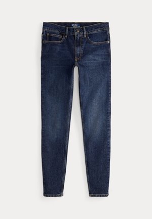 Mörkblå slim-fit jeans med framfickor, bältesöglor och stängning med knapp, liggande platt på en ljus bakgrund.