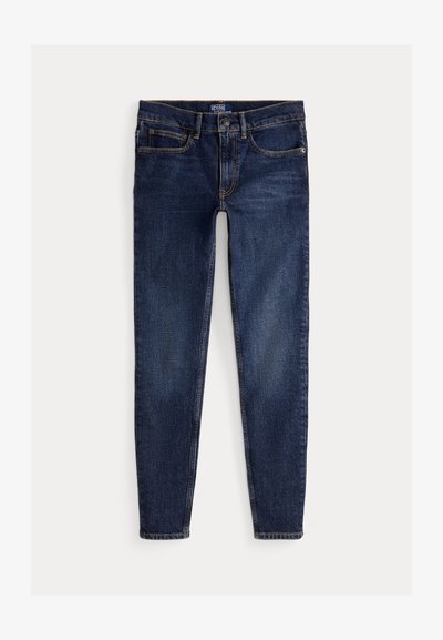 Temno modri slim-fit kavbojke z sprednjimi žepi, pasnimi zankami in gumbom, razporejene na svetlem ozadju.