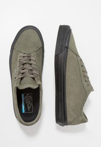 Plátěné tenisky olivově zelené barvy s černými gumovými podrážkami. Mají ploché tkaničky, zesílené švy a polstrovanou stélku.