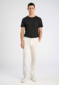 Zwarte short-sleeve t-shirt, relaxed fit, gecombineerd met licht beige linnen broek met zakken, gedragen met witte sneakers.