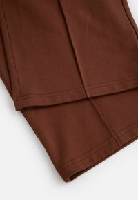 Brązowa bawełniana tkanina o gładkiej fakturze, z starannie wykonanymi szwami i zawiniętym dołem. Projekt jest prosty i niewyszukany.