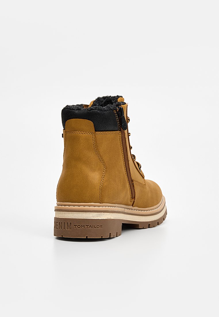 Tawny enkelboots met een glad leren bovenwerk, zwarte bontvoering, een zijrits en een dikke rubberen zool met het opschrift "DENIM TOM TAILOR."