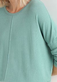 Ljus teal oversized tröja i mjukt stickat material. Har en rund halsringning och ribbade ärmar med en subtil sömdetalj framtill.