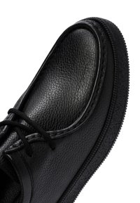 Zwarte leren schoen met een textuur, ronde neus en vetersluiting. De zool is van rubber met een geprofileerd patroon voor grip.