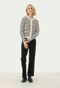 Raidallinen neulecardigan vaaleassa ja tummansinisessä, neulotut pinnat, pyöreä pääntie, nappisuljenta, kaksi etutaskua, yhdistettynä mustiin housuihin ja kenkiin.