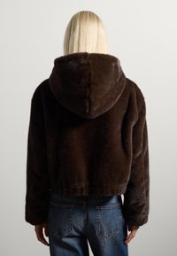 Sudadera de piel sintética marrón con una textura suave y capucha, combinada con jeans de mezclilla azul de tiro alto. Presenta un diseño cortado y un ajuste relajado.
