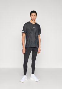 Camiseta deportiva negra que absorbe la humedad, con un diseño texturizado y acentos blancos, combinada con mallas negras ajustadas y zapatillas blancas.