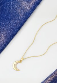 Collana d'oro con pendente a forma di luna crescente decorato con gemme trasparenti, sullo sfondo scintillante blu e bianco.