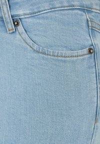 Lichtblauwe denim jeans met een zichtbare voorzak, geaccentueerd met subtiele gouden stiksels en een decoratieve metalen knop.